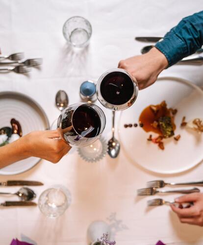 Two people seated at a table toast with glasses of red wine