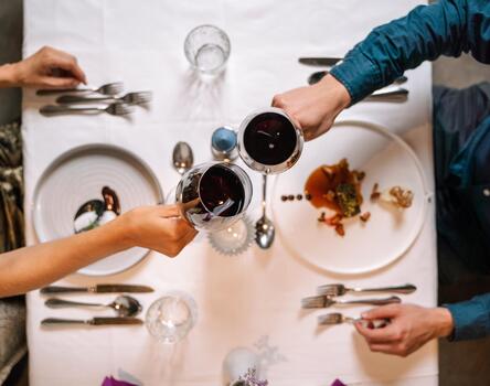 Two people seated at a table toast with glasses of red wine