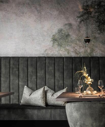 Modern, dark seating area with a gray couch, two small wooden tables, decorative flower arrangements, and a mood-lit wall in the background.