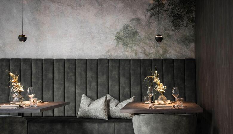 Modern, dark seating area with a gray couch, two small wooden tables, decorative flower arrangements, and a mood-lit wall in the background.