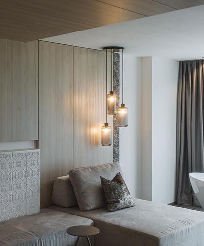 Modernly furnished room with a freestanding bathtub, sofa, dresser, and large windows letting in natural light.