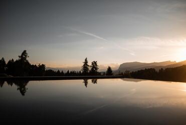 In primo piano la piscina al tramonto; sullo sfondo si vedono boschi e montagne.