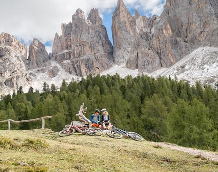 Un uomo e una donna siedono su un prato alpino davanti alle Dolomiti