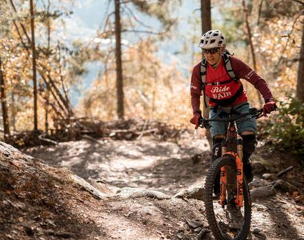 A mountain biker rides along a narrow forest trail through autumn leaves