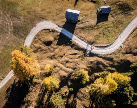 Veduta aerea di una pista ciclabile sinuosa che attraversa un paesaggio con alberi in fiore gialli e due baite alpine