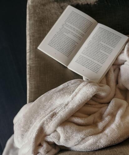Nahaufnahme eines Sessels mit einer hellbraunen Decke und einem aufgeschlagenen Buch.