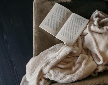 Nahaufnahme eines Sessels mit einer hellbraunen Decke und einem aufgeschlagenen Buch.