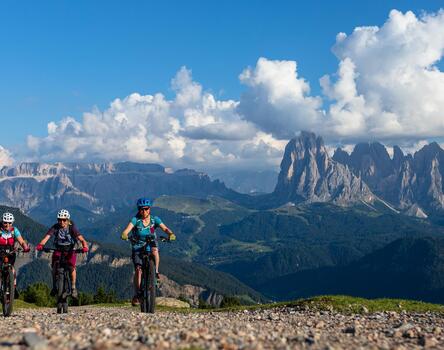 Three women ride their bicycles uphill in the Dolomites