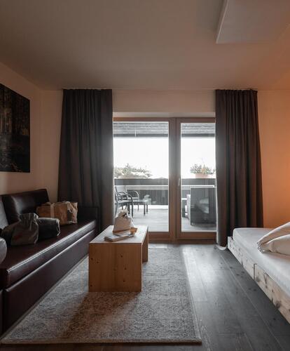 Modernes Hotelzimmer im Bikehotel Pfösl mit Bett, Ledersofa, Holztisch und Balkon.