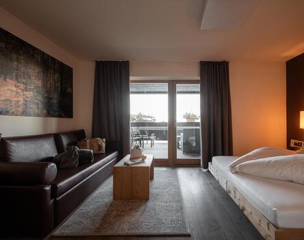 Modernes Hotelzimmer im Bikehotel Pfösl mit Bett, Ledersofa, Holztisch und Balkon.