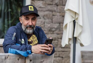 Un uomo è seduto su una panchina di legno e tiene uno smartphone in mano