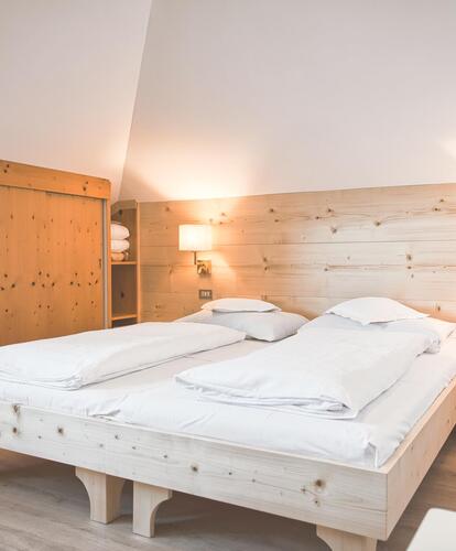 Camera da letto luminosa con un letto matrimoniale, coperte bianche e rivestimento in legno, illuminata da una lampada da parete.