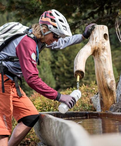 Ciclista con pantaloni rossi e casco che attinge acqua da un pozzo di legno nella natura