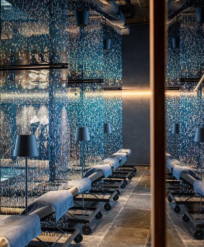 Primo piano di un'area benessere moderna con piscina interna, lettini, grandi finestre in vetro e pavimento scuro.