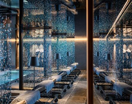 Primo piano di un'area benessere moderna con piscina interna, lettini, grandi finestre in vetro e pavimento scuro.