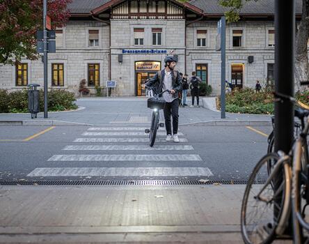 Un uomo attraversa la strada con la sua bicicletta, sullo sfondo la stazione ferroviaria di Bressanone