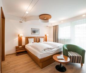 Camera d'hotel moderna e luminosa con letto matrimoniale, lampade da comodino, una poltrona, un piccolo tavolo rotondo e una grande vetrata.