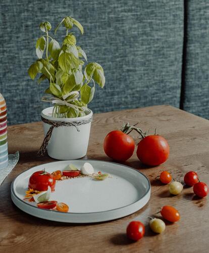 Close-up of a table: on it are tomatoes, a colorful striped bottle, and a basil plant.