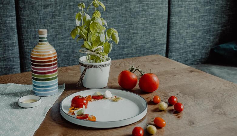 Close-up of a table: on it are tomatoes, a colorful striped bottle, and a basil plant.
