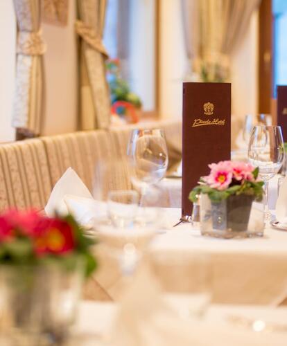 The dining room of Hotel Piccolo with tables set with menu cards, small floral arrangements, wine glasses, napkins and cutlery.