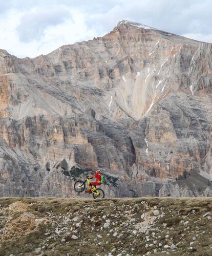 A cyclist on rocky terrain; an impressive mountain range in the background.