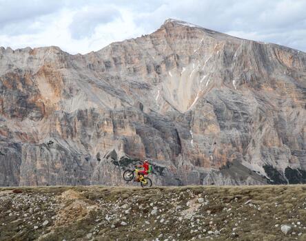 A cyclist on rocky terrain; an impressive mountain range in the background.