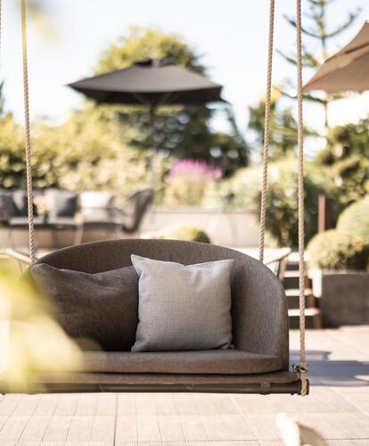 Terrazza soleggiata con poltrone lounge imbottite e ombrellone, circondata da piante e con vista sul giardino.