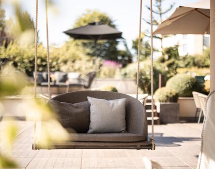 Terrazza soleggiata con poltrone lounge imbottite e ombrellone, circondata da piante e con vista sul giardino.