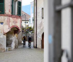 Two cyclists ride through a narrow alley