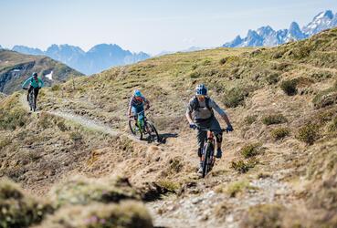 Drei Mountainbiker fahren einen Trail in Sexten
