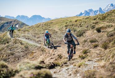 Drei Mountainbiker fahren einen Trail in Sexten