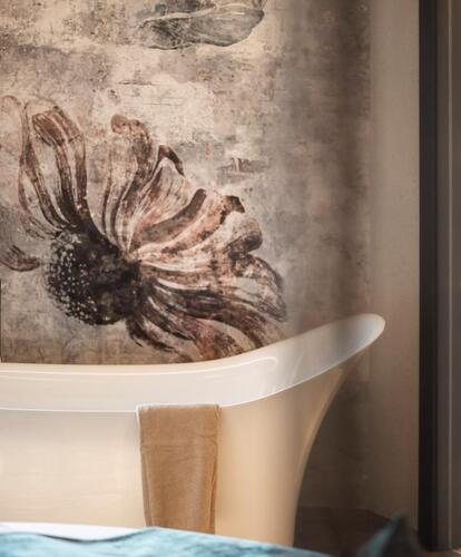 Camera d’hotel moderna con vasca da bagno freestanding davanti a una parete in pietra, motivo decorativo a parete, letto in primo piano e area bagno illuminata.