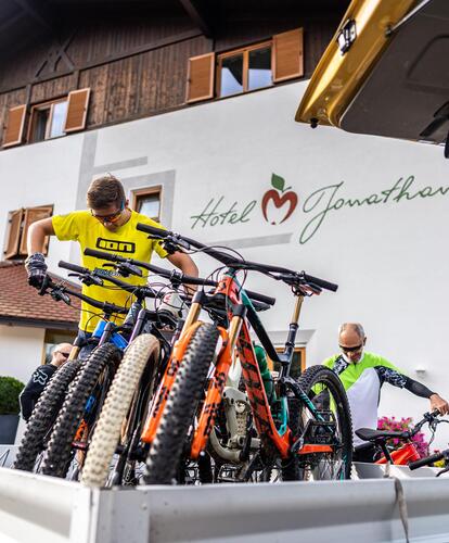 Diverse biciclette sul cassone di un furgone davanti all’Hotel Jonathan; sullo sfondo persone in abbigliamento da ciclismo e casco.