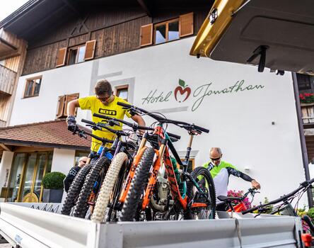 Diverse biciclette sul cassone di un furgone davanti all’Hotel Jonathan; sullo sfondo persone in abbigliamento da ciclismo e casco.