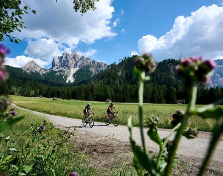 Due mountain biker pedalano su una pista ciclabile, circondati dalle Dolomiti