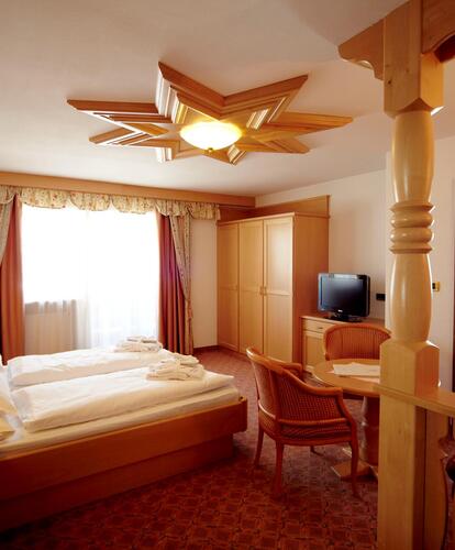 Hotel room at Hotel Piccolo with a double bed, wooden furniture and a sitting area; on the right, the bathroom can be seen through an open door.