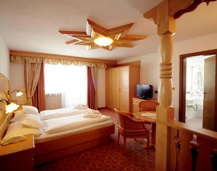Hotel room at Hotel Piccolo with a double bed, wooden furniture and a sitting area; on the right, the bathroom can be seen through an open door.