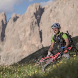 L'ospite Gunther Linder è seduto accanto alla sua bicicletta su un prato; sullo sfondo si vedono le possenti Dolomiti.