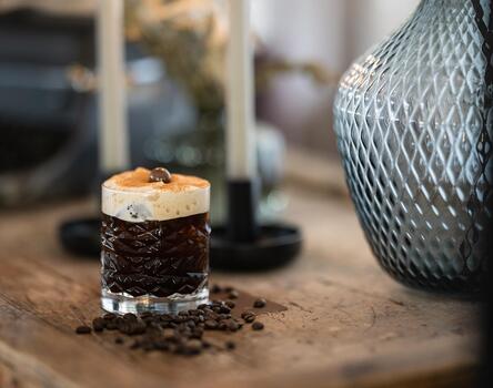 Piccolo dessert con crema chiara su un tavolo in legno, accanto a tracce di caffè, una candela e un vaso blu strutturato.