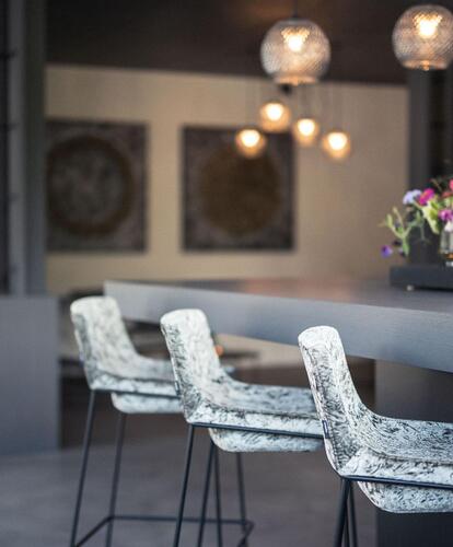 Modern hotel bar area with illuminated counter, high stools, hanging lamps, and flowers on the counter.