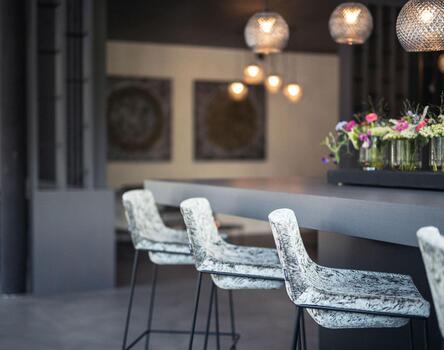 Modern hotel bar area with illuminated counter, high stools, hanging lamps, and flowers on the counter.