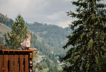 Frau auf Balkon vor Wald und Bergen