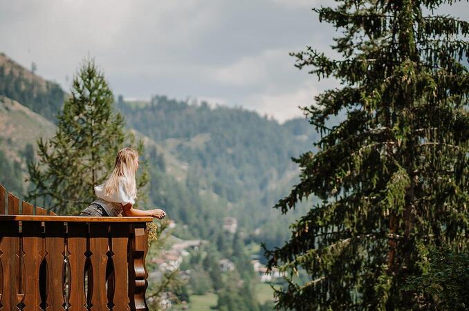 Frau auf Balkon vor Wald und Bergen