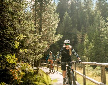Una donna e un uomo attraversano in bicicletta un ponte nel bosco