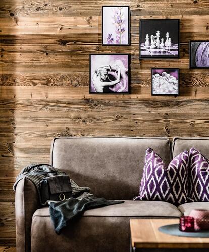 Camera d’hotel accogliente e arredata in stile moderno con divano in pelle marrone davanti a una parete in legno, cornici decorative, tavolino e lampada a sospensione.