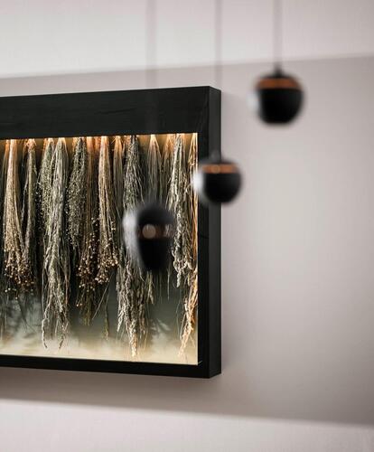 Abstract wall art with vertically hanging bundles of herbs, above which hang three round black pendant lights in front of a white wall.