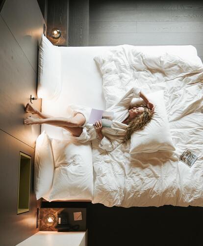 Modernes Hotelzimmer; Eine Frau im weißen Bademantel liegt auf einem Bett mit dunkeln Boden und Wänden.