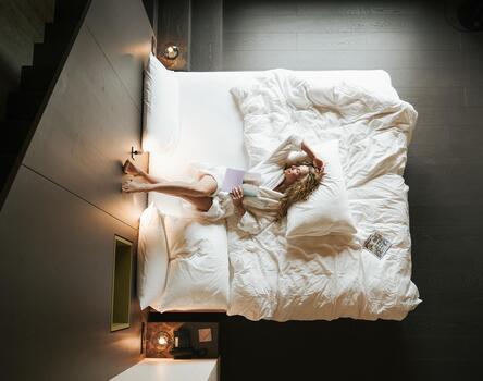 Modernes Hotelzimmer; Eine Frau im weißen Bademantel liegt auf einem Bett mit dunkeln Boden und Wänden.