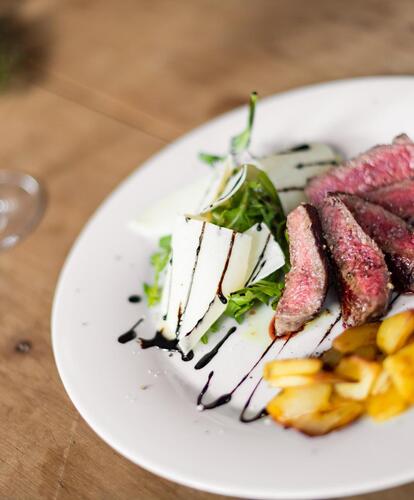 Primo piano di un tavolo con un piatto contenente un piatto di carne, accanto un bicchiere di vino rosso.