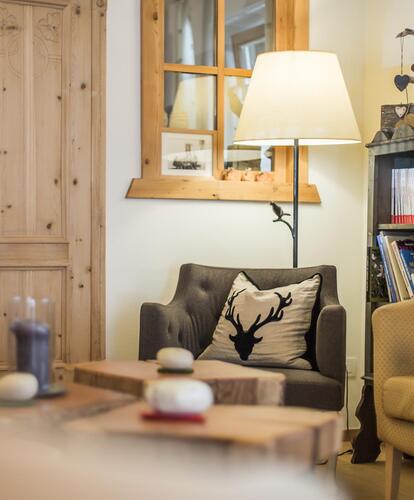 Una zona accogliente con poltrone, piccoli tavoli, una lampada da terra, un armadio in legno e una libreria.